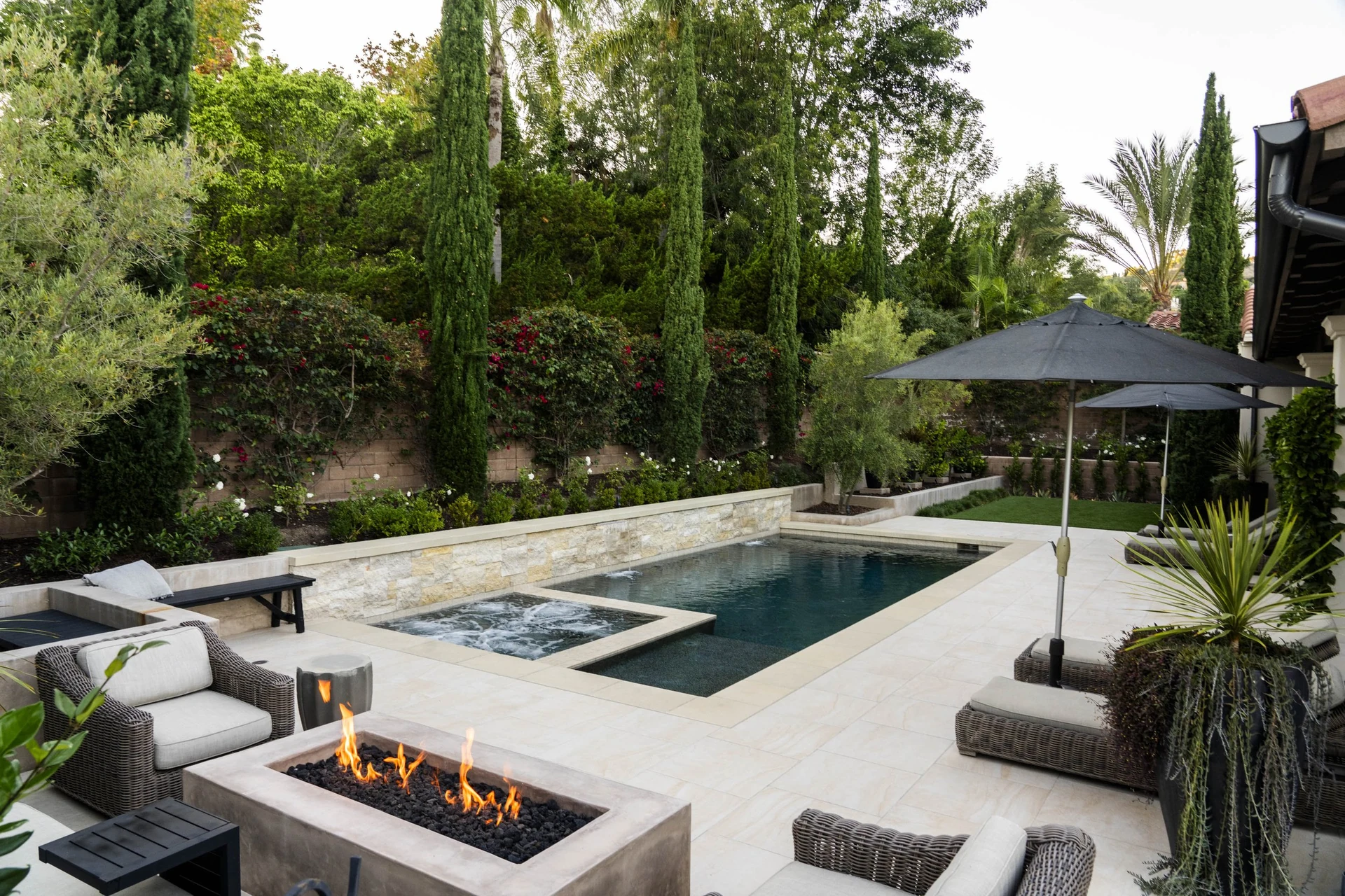 Fire pit lounge beside the pool and spa, with cypress and planting.