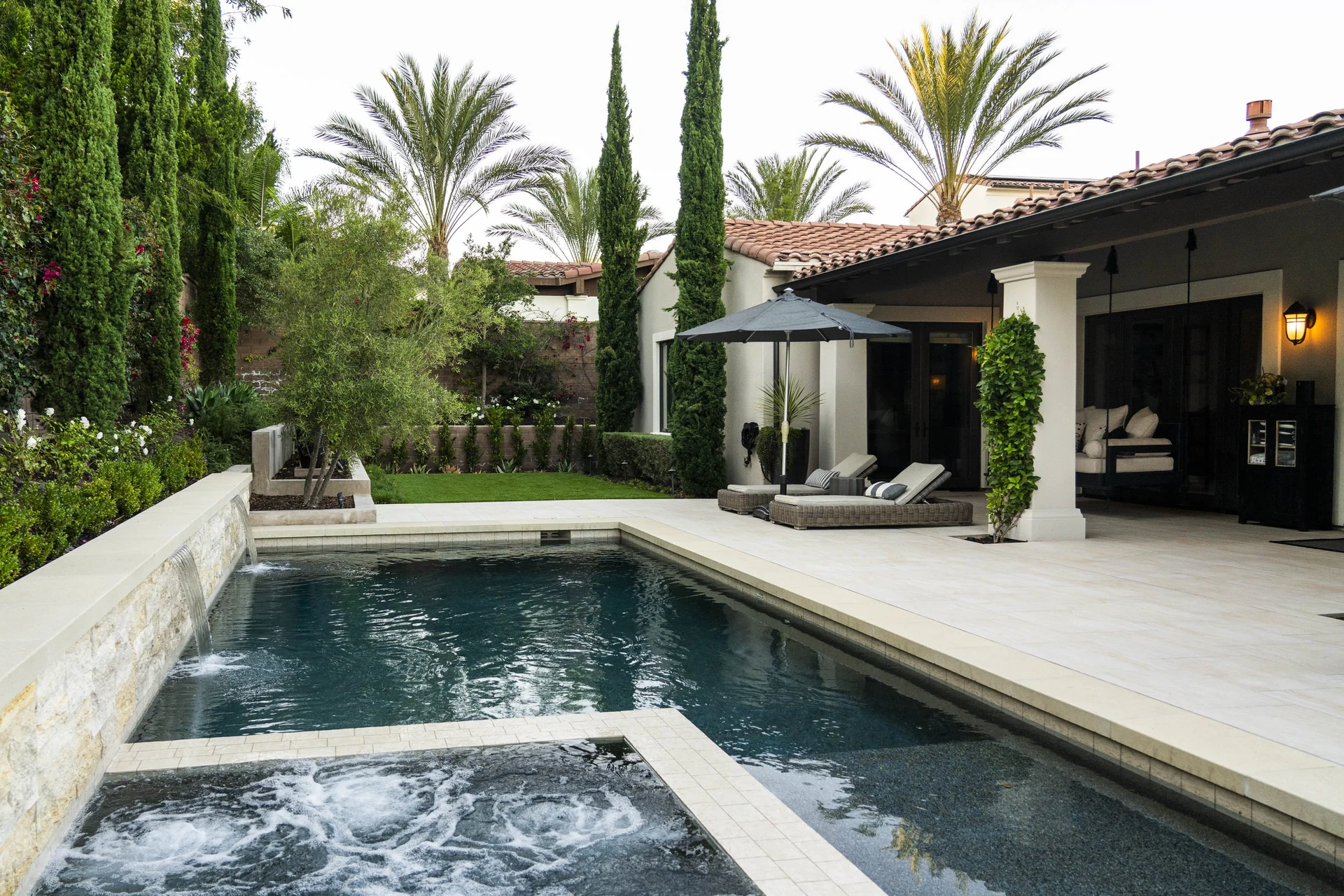 Pool and attached spa with pale stone decking and cypress planting.