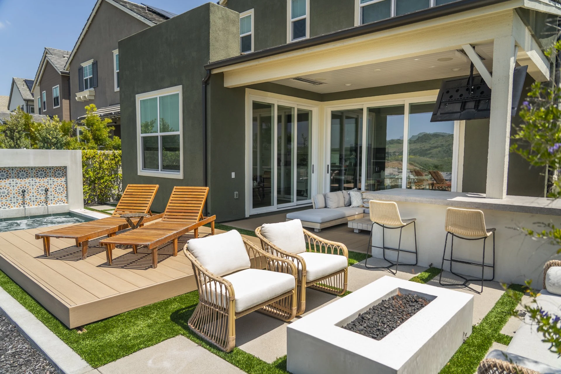 Deck with chaises, a white fire table, tiled water wall and covered patio.